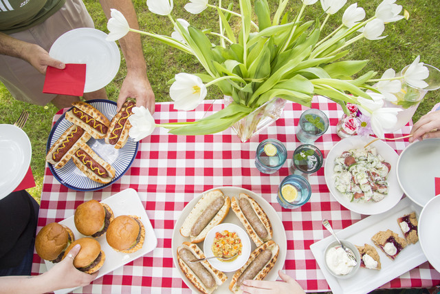 spread of grilled burgers and hot dogs and potato salad and dessert on a checkered cloth lined table with h make their plate